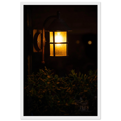 Glowing vintage lantern mounted on a wooden pole in front of a bush at night on wooden framed wall art