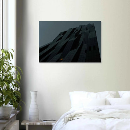 Black and white low angle view of a modern skyscraper with bold geometric lines and dark textured facade on Canvas Print wall art on the wall in the Bedroom