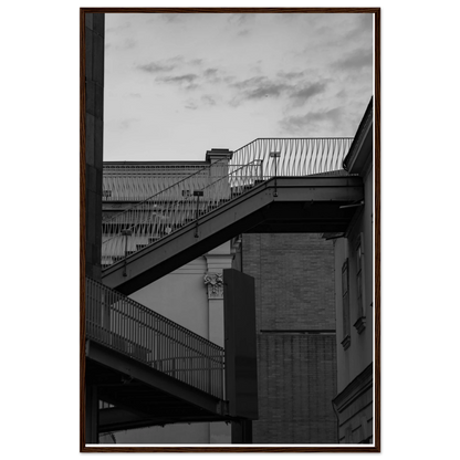 Black and white photo on a wooden frame wall art of an outdoor staircase connecting two buildings under a dramatic cloudy sky