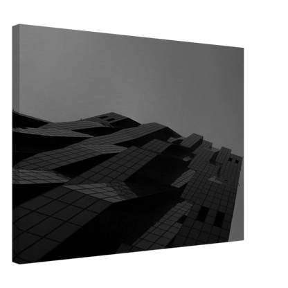 Black and white low angle view of a modern skyscraper with bold geometric lines and dark textured facade on Canvas Print wall art