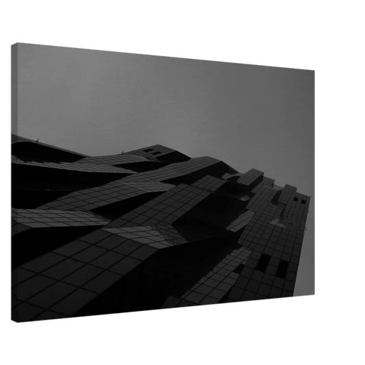 Black and white low angle view of a modern skyscraper with bold geometric lines and dark textured facade on Canvas Print wall art