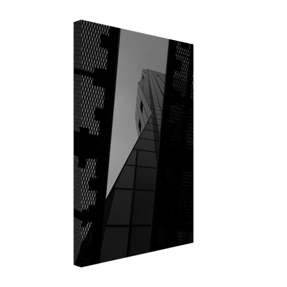 Black and white Low angle view looking up at a tall glass skyscraper framed between two metal structural elements on Canvas Print wall art
