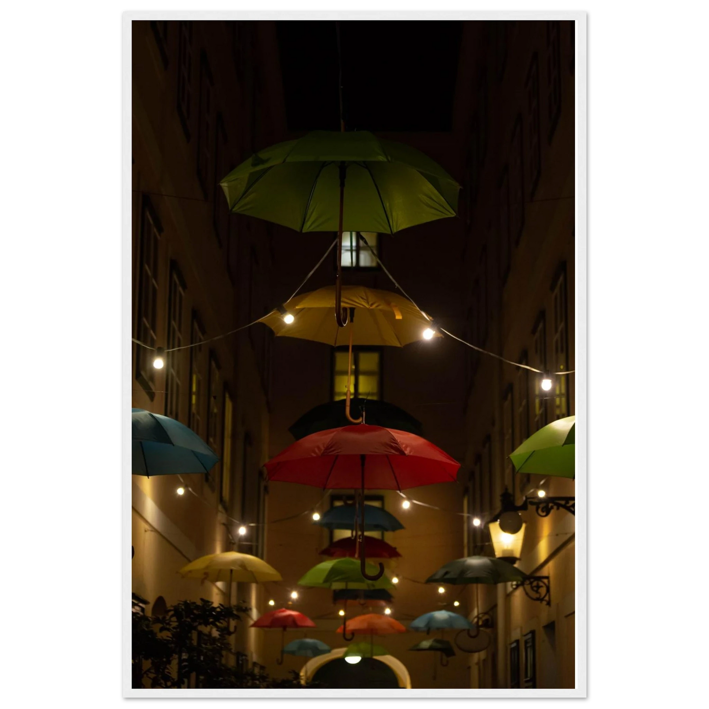 Nighttime street scene with colorful illuminated umbrellas hanging as decoration above a vibrant outdoor area on a wooden frame wall art