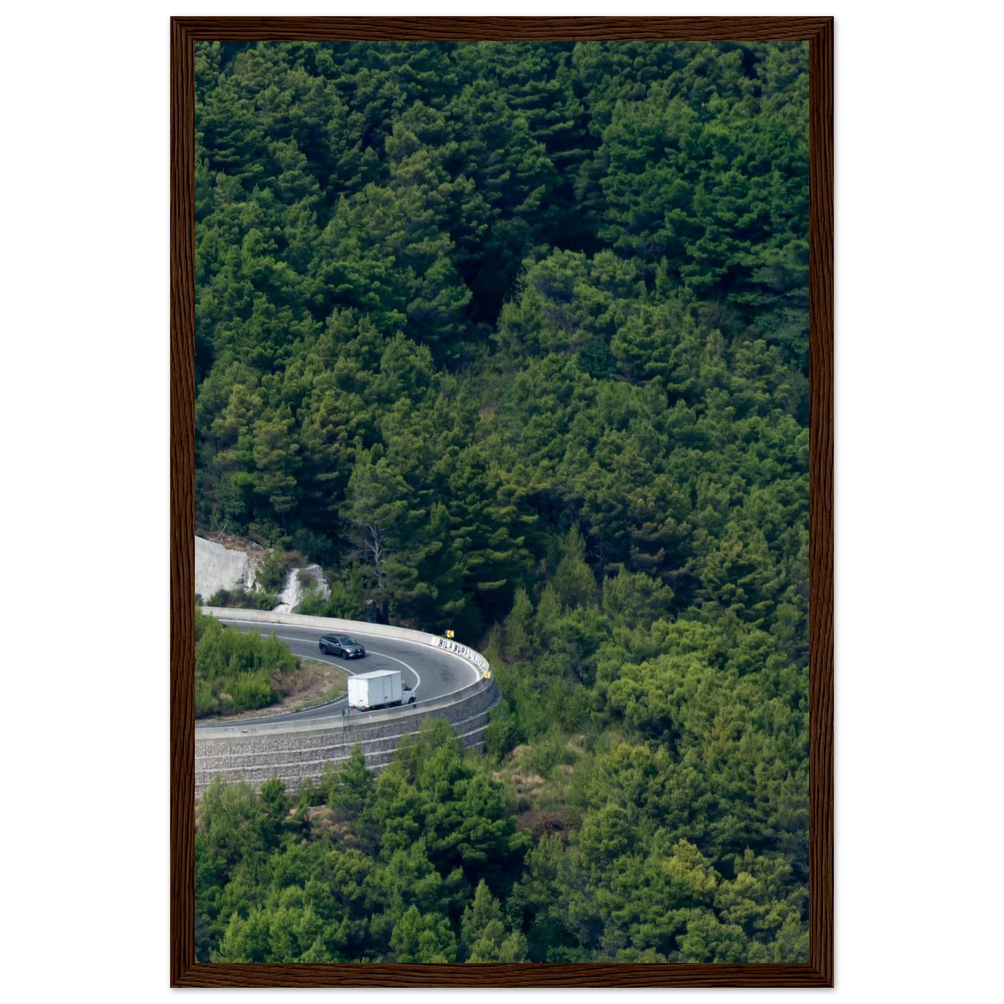 Aerial view of a winding road curve with cars surrounded by lush green forest landscape on wooden framed wall art