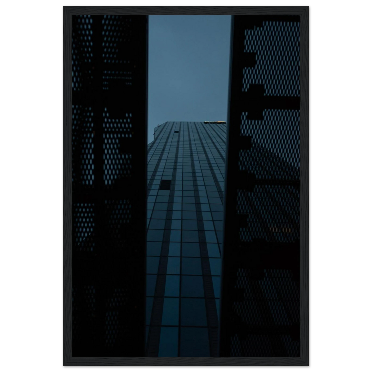Low angle view looking up at a tall glass skyscraper framed between two metal structural elements on wooden framed wall art