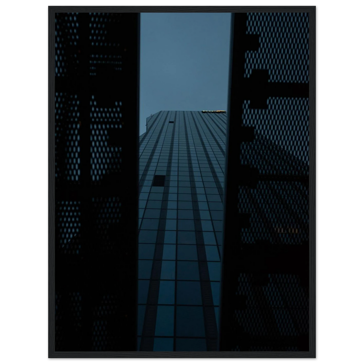 Low angle view looking up at a tall glass skyscraper framed between two metal structural elements on wooden framed wall art