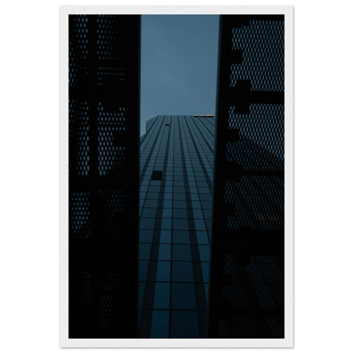 Low angle view looking up at a tall glass skyscraper framed between two metal structural elements on wooden framed wall art