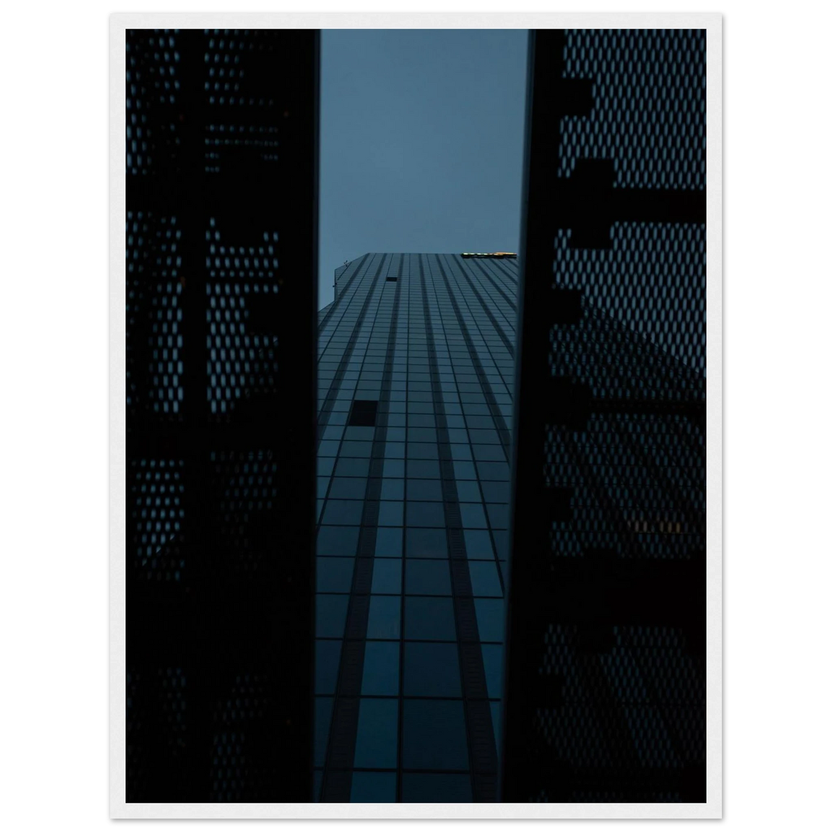 Low angle view looking up at a tall glass skyscraper framed between two metal structural elements on wooden framed wall art