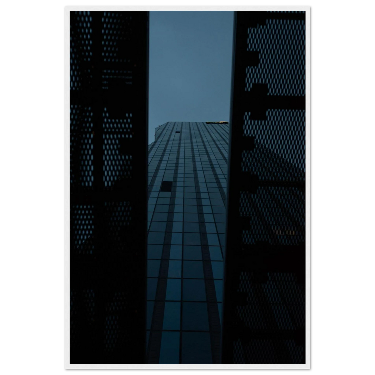 Low angle view looking up at a tall glass skyscraper framed between two metal structural elements on wooden framed wall art