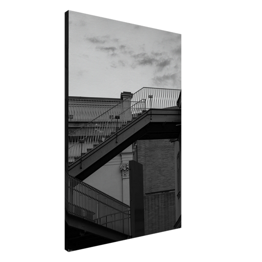 Black and white photo on a Canvas Print wall art of an outdoor staircase connecting two buildings under a dramatic cloudy sky
