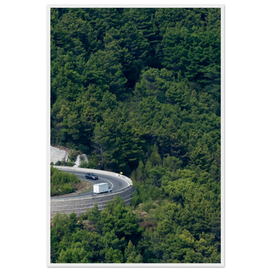 Aerial view of a winding road curve with cars surrounded by lush green forest landscape on wooden framed wall art
